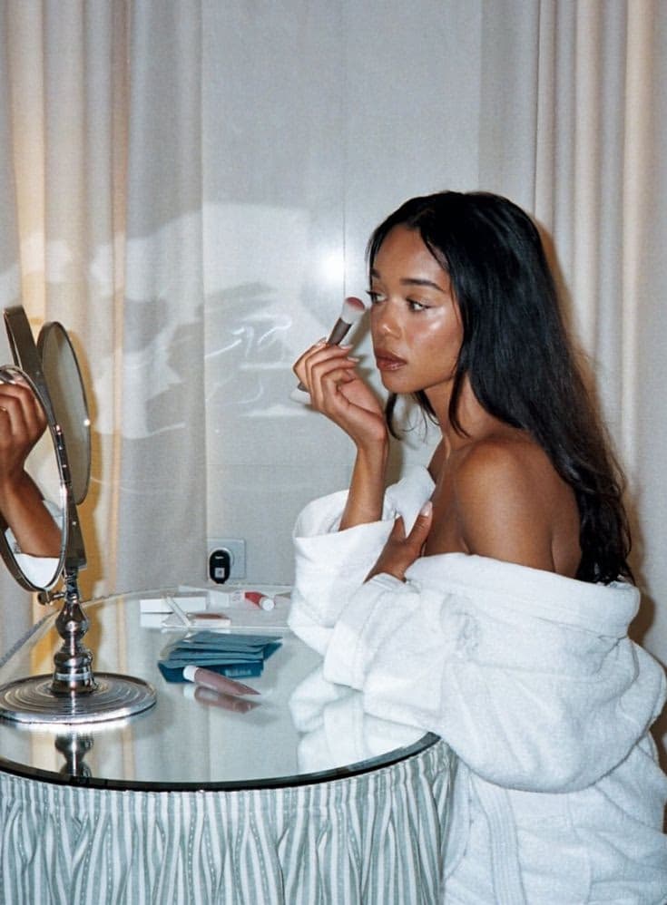 Woman applying makeup with a brush in front of a vanity mirror, self makeup class in Dubai with Elani